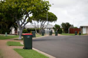 Rubbish bin with red lid and recycling bins on the street.
