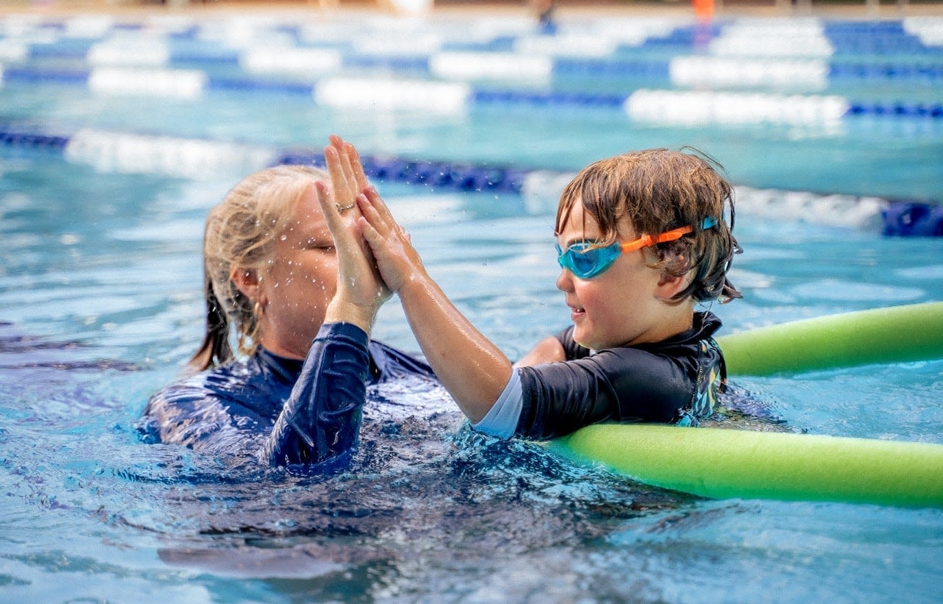Swim teacher high fiving a young student in a pool
