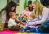 A group of mothers and their toddlers are sitting together at preschool and are playing with toys.