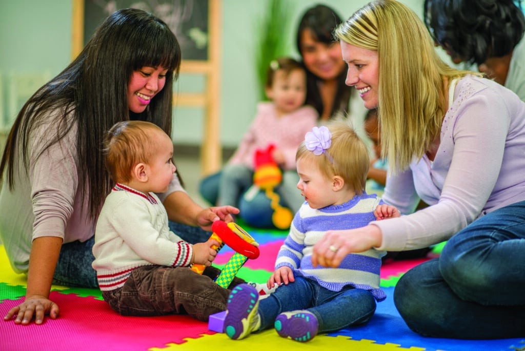 A group of mothers and their toddlers are sitting together at preschool and are playing with toys.