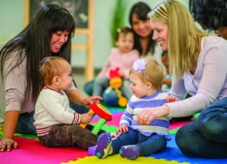 A group of mothers and their toddlers are sitting together at preschool and are playing with toys.