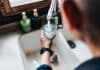 Over the shoulder view of senior Asian man filling a glass of filtered water right from the tap in the kitchen at home