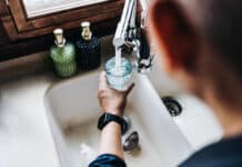 Water meter reading underway soon Over the shoulder view of senior Asian man filling a glass of filtered water right from the tap in the kitchen at home